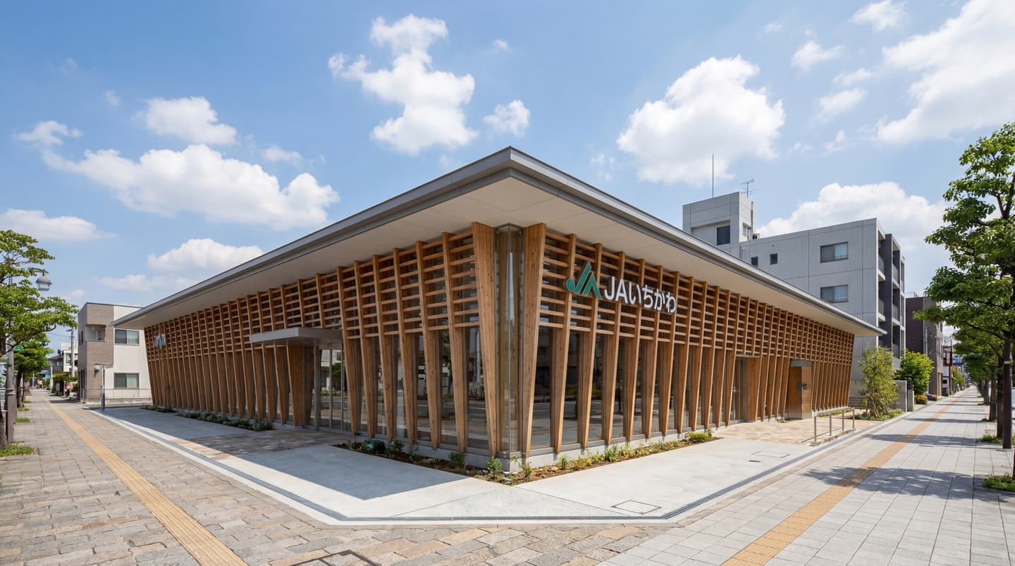 青空の下、木製ルーバーとガラス張りのモダンなデザインが特徴的なJAいちかわの店舗外観パース。角地に建つ平屋の建物で、木材の縦格子がファサード全体を覆い、洗練された温かみのある印象を与える建築デザイン。
